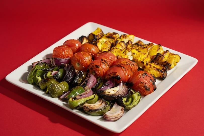 Grilled chicken, tomatoes, green peppers, and red onions arranged on a white rectangular plate.