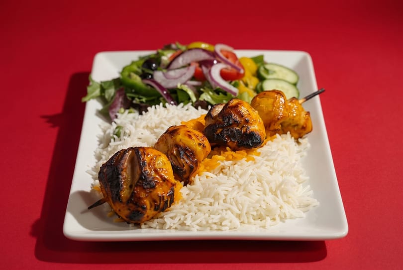 Grilled chicken skewers with white rice and a fresh garden salad on a white plate.
