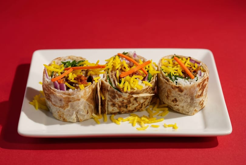 Three colorful burritos filled with rice, red onion, carrots, and yellow rice on a white plate.