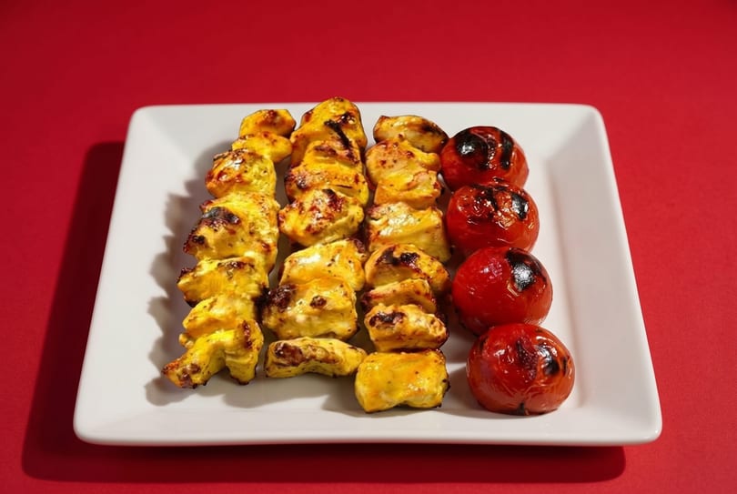 Three skewers of grilled chicken and one skewer of grilled tomatoes on a white rectangular plate.