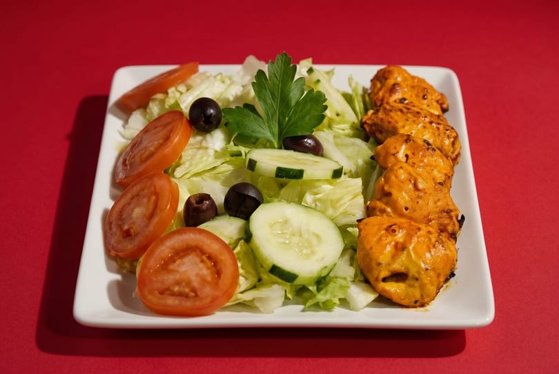 Chicken tikka skewers with a side salad of lettuce, tomatoes, cucumbers, olives, and parsley.